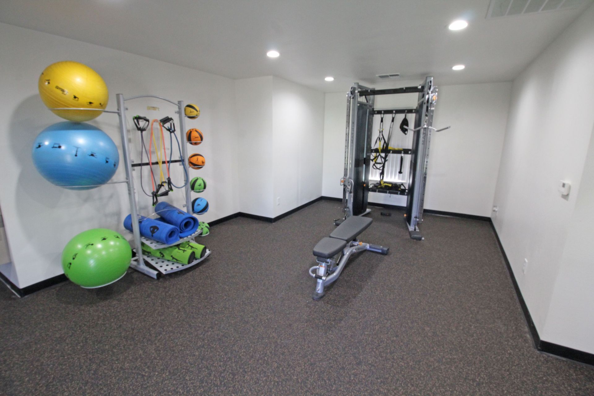A gym with a bench , exercise balls , and a machine.