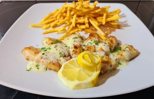 Filets de poulet sauce citron et frites sur une assiette blanche, garnis d'un zeste de citron.
