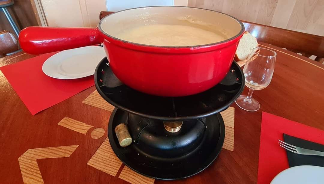 Caquelon à fondue rouge avec fromage fondu sur le brûleur, table dressée pour le dîner.