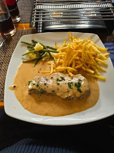 Assiette avec steak en sauce, frites et haricots verts; posée sur une table.
