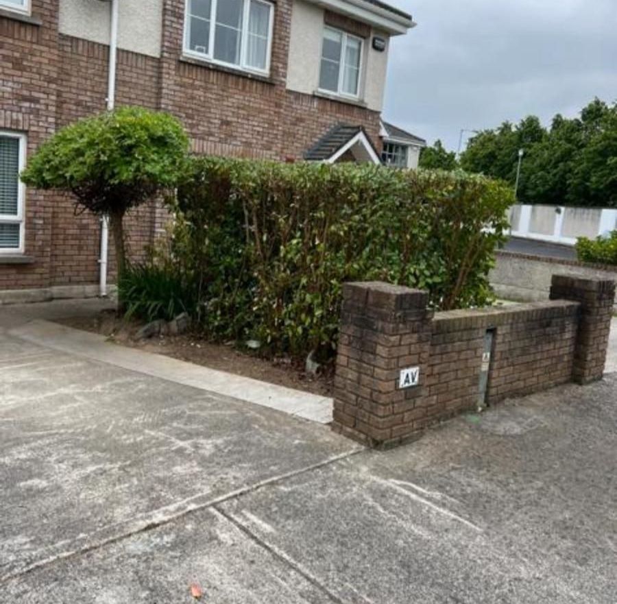 A brick wall surrounds a lush green garden in front of a brick house.