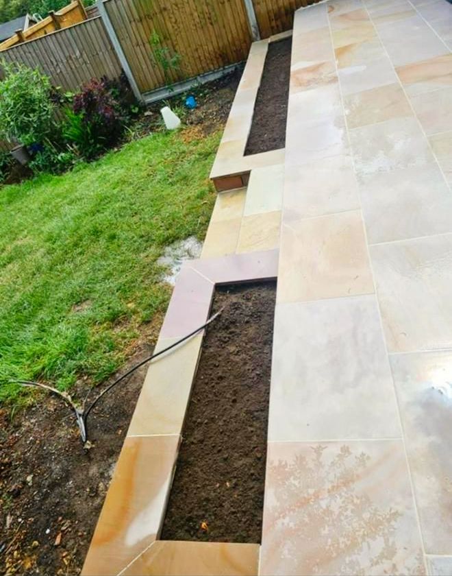 A stone patio with built-in rectangular planters filled with soil next to a lawn.
