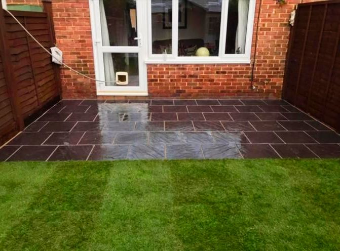 Brick house with dark stone patio, door, and green lawn.