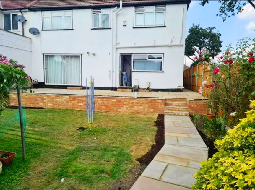 Backyard with house and garden, featuring brickwork, lawn, and stone path.
