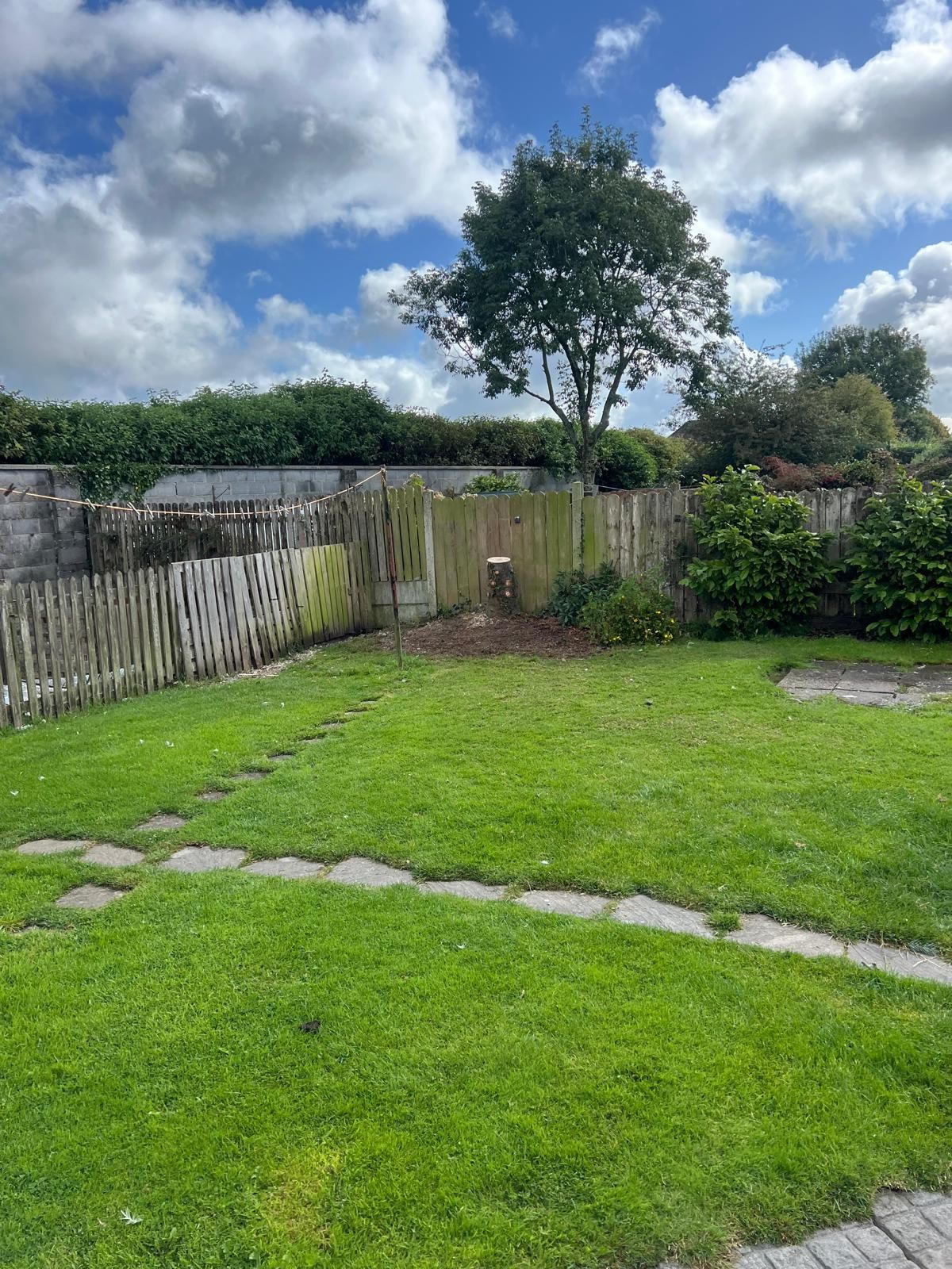 Green grassy backyard with a picket fence, stone path, and tree under a cloudy sky.