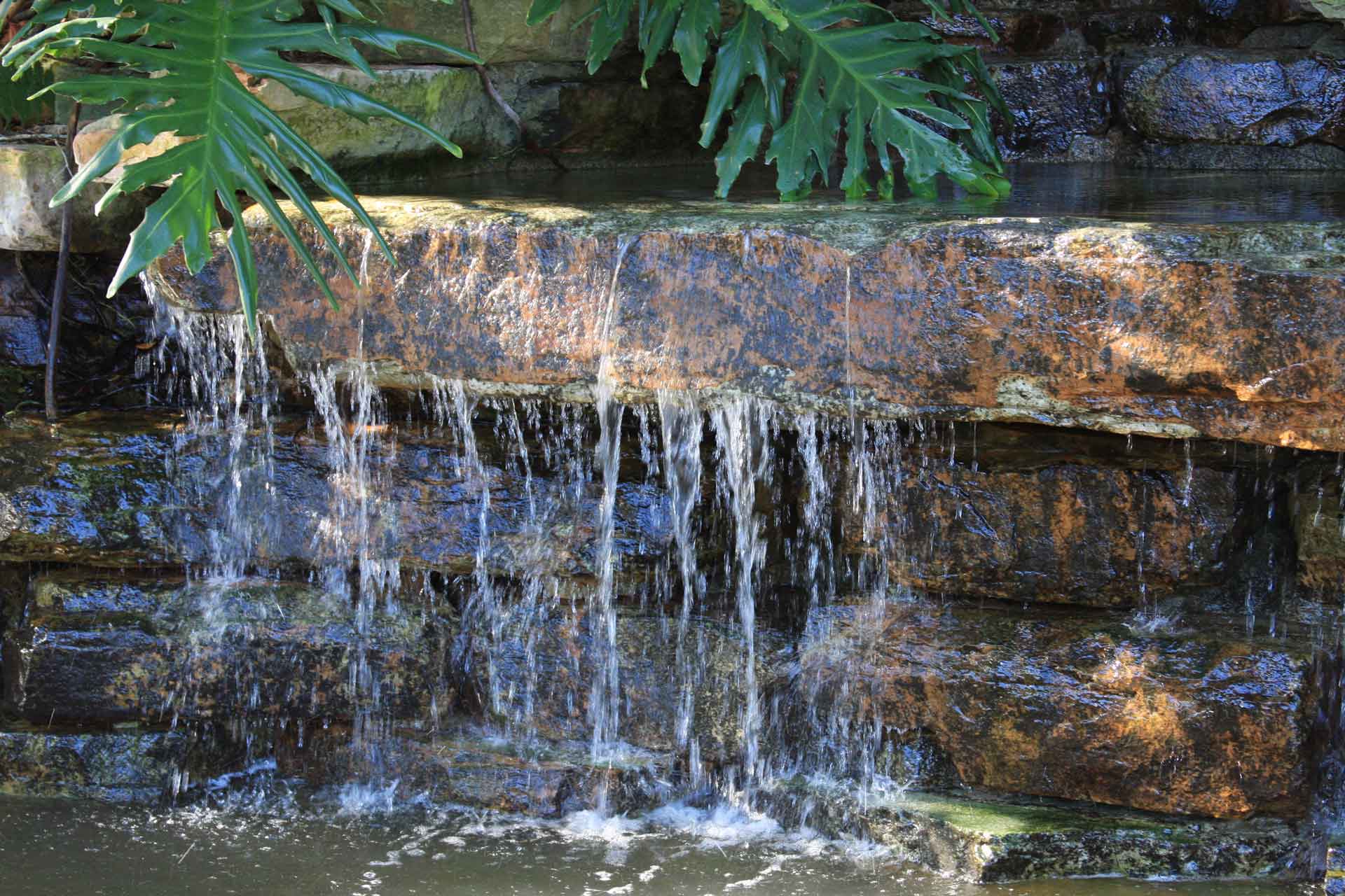 Small waterfall cascading over layered brown stones, with green leaves above.