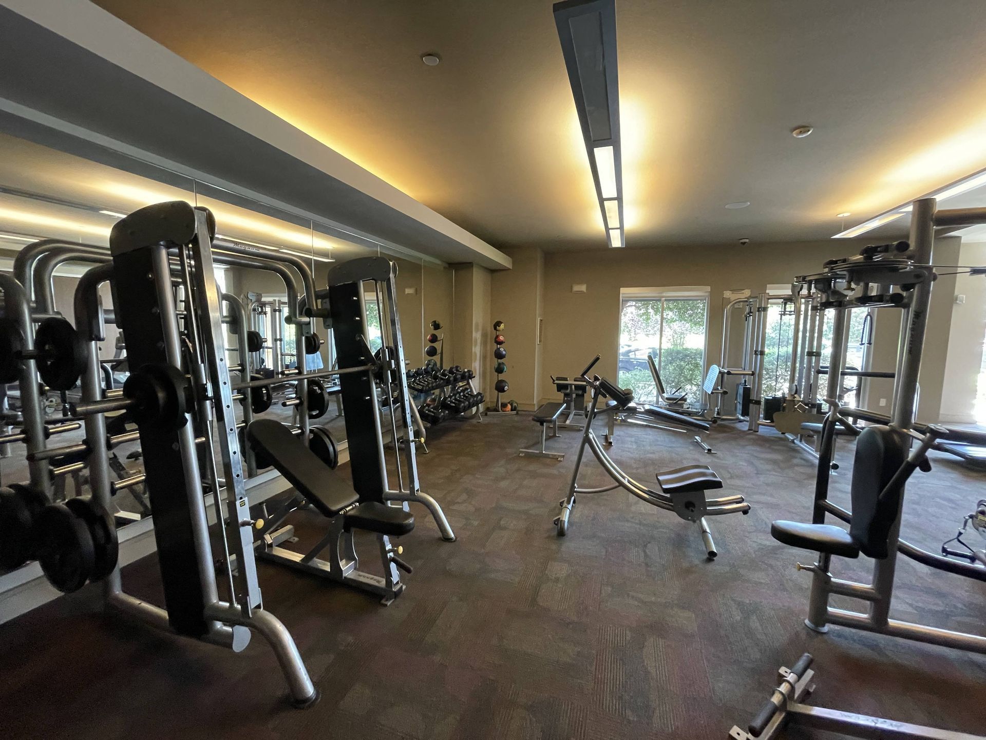 a gym with weights and cardio equipment on the floor and a window