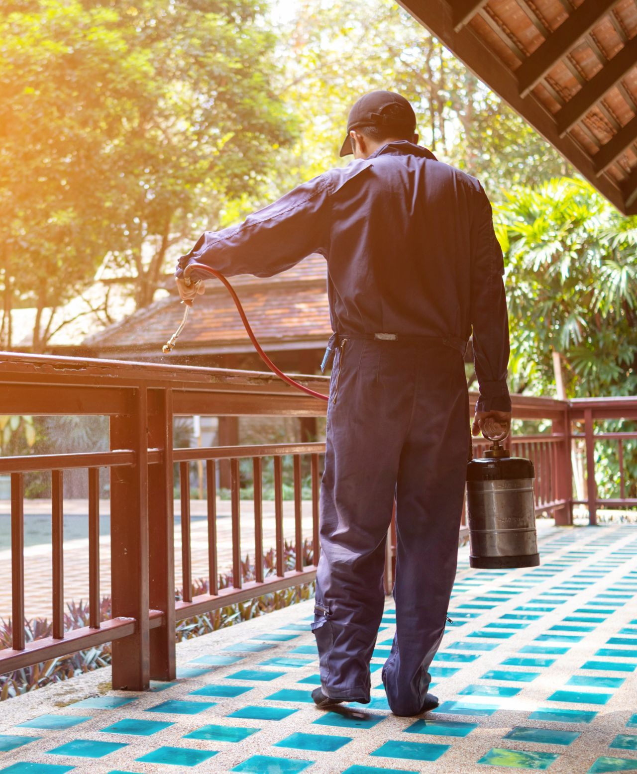 A man is spraying insecticide on a balcony with a sprayer.