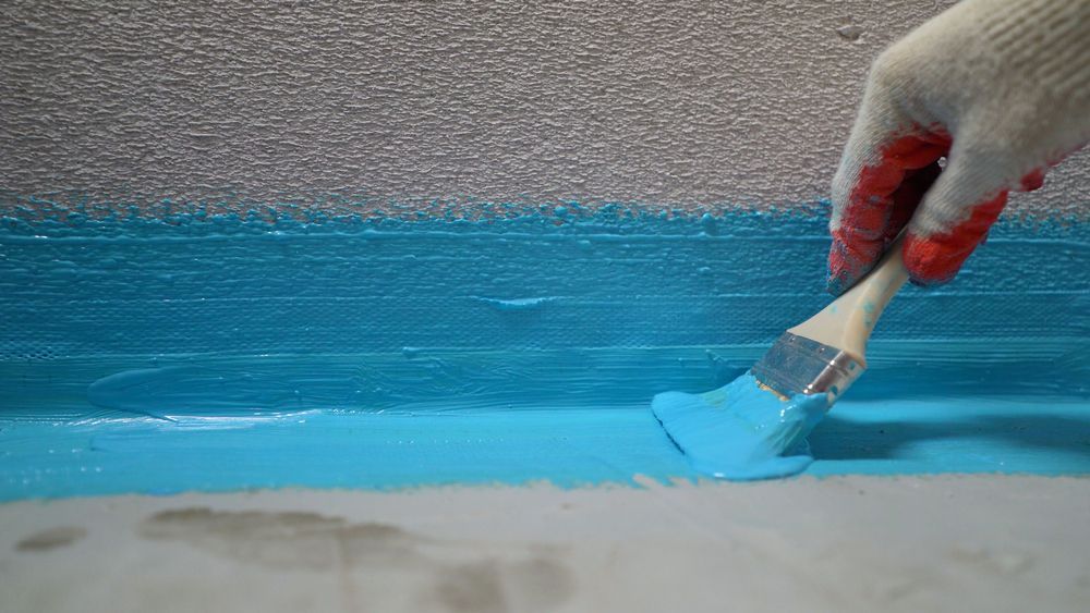 A person is painting a blue wall with a brush.