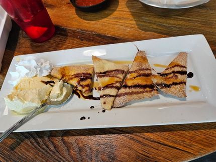 Dessert platter with sliced crepes, whipped cream, and ice cream on a white plate at a wooden table