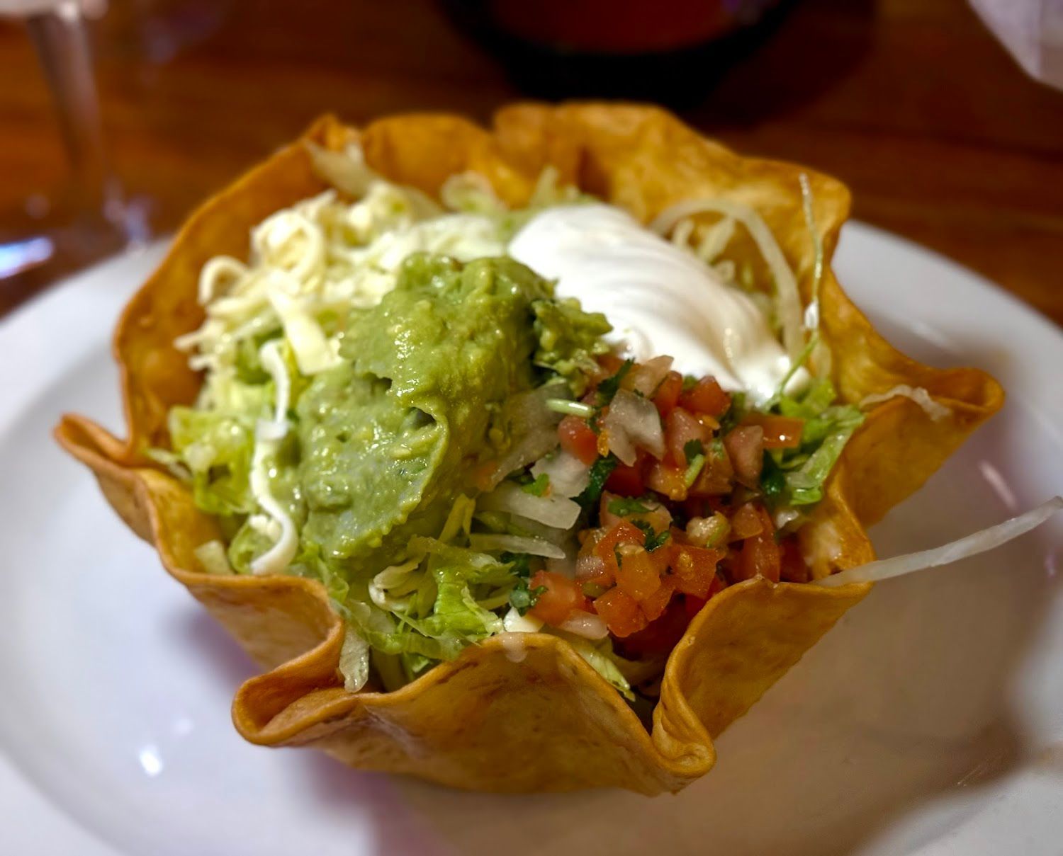 Taco salad in a crispy tortilla bowl topped with guacamole, sour cream, lettuce, and salsa