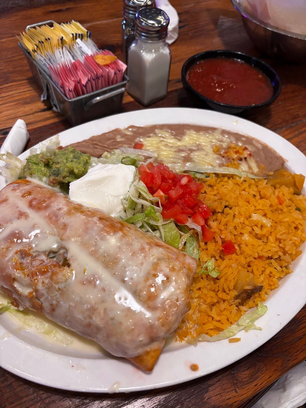 Plate of Mexican food with burrito, rice, beans, lettuce, sour cream, salsa, and chips on a table