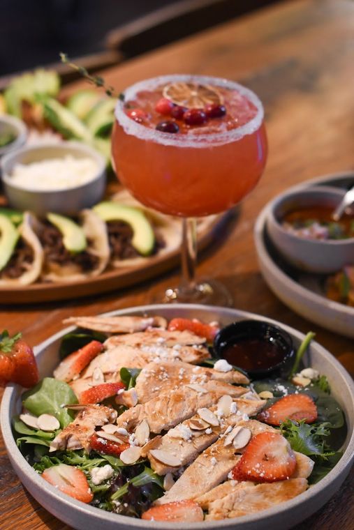 Salad bowl with strawberries and avocado beside a red cocktail in a restaurant setting