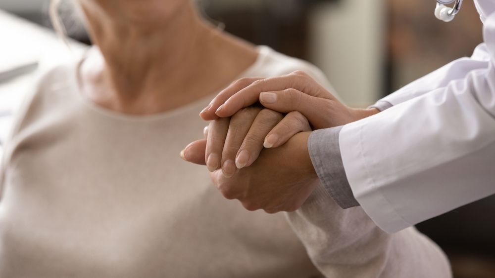 A medical professional in a white coat holds a person’s hand in a gesture of support and care.