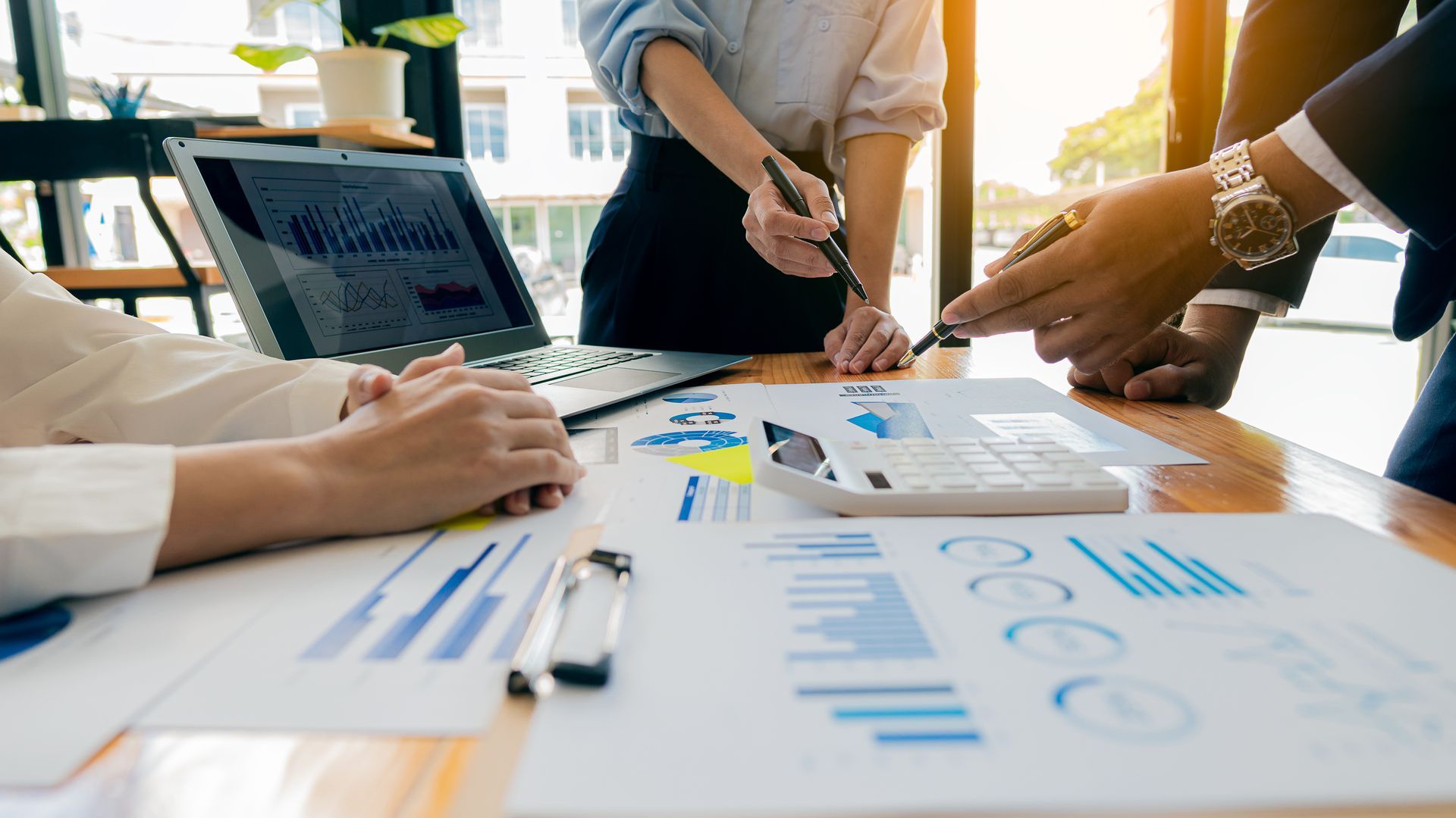 People in business attire reviewing financial documents at a desk, laptop open with graphs.