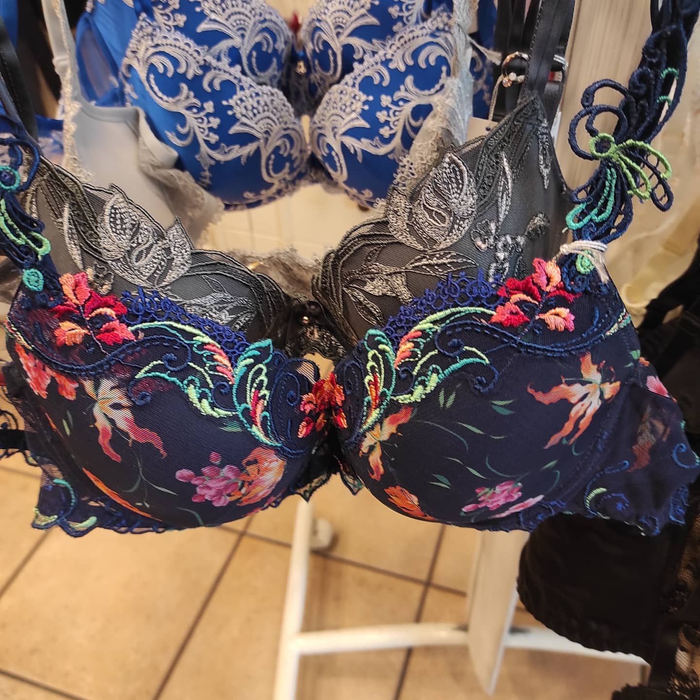 Primo piano di reggiseni blu navy e con ricami floreali esposti su una mensola bianca.