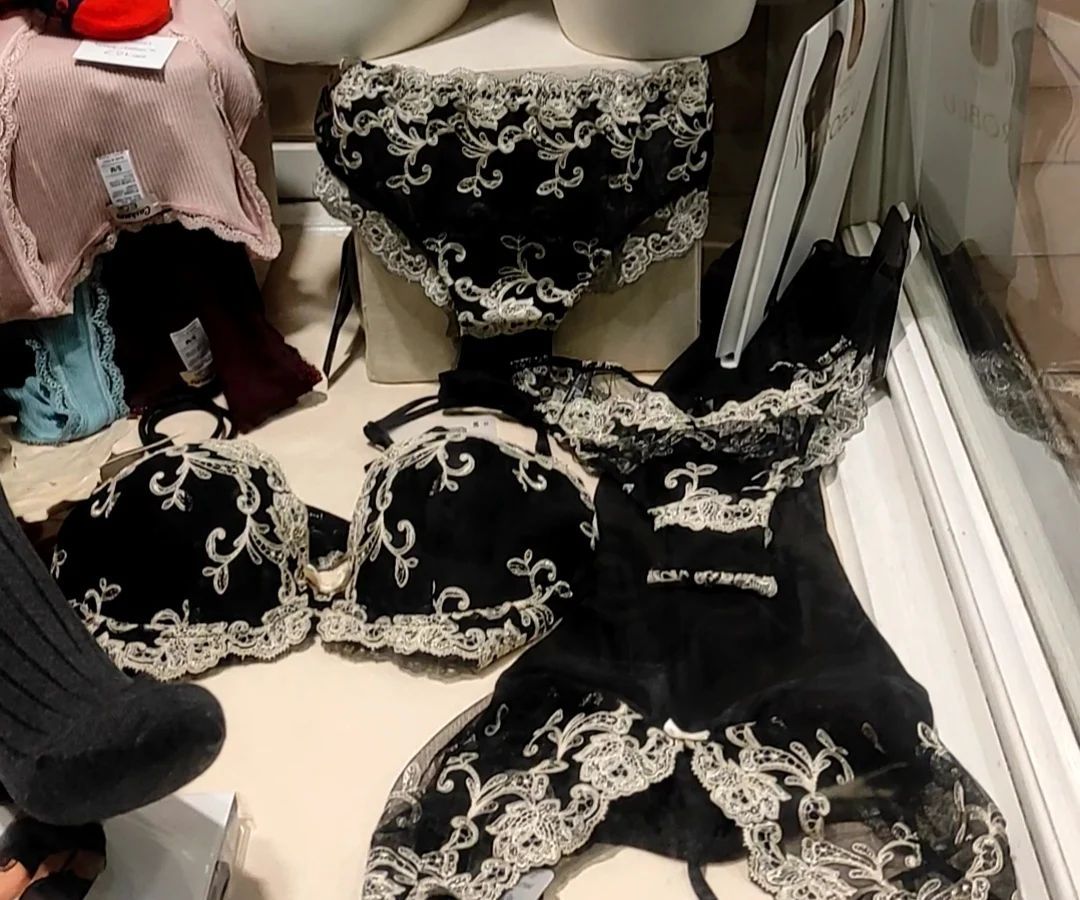 Completo intimo nero con rifiniture in pizzo bianco, esposto nella vetrina di un negozio.
