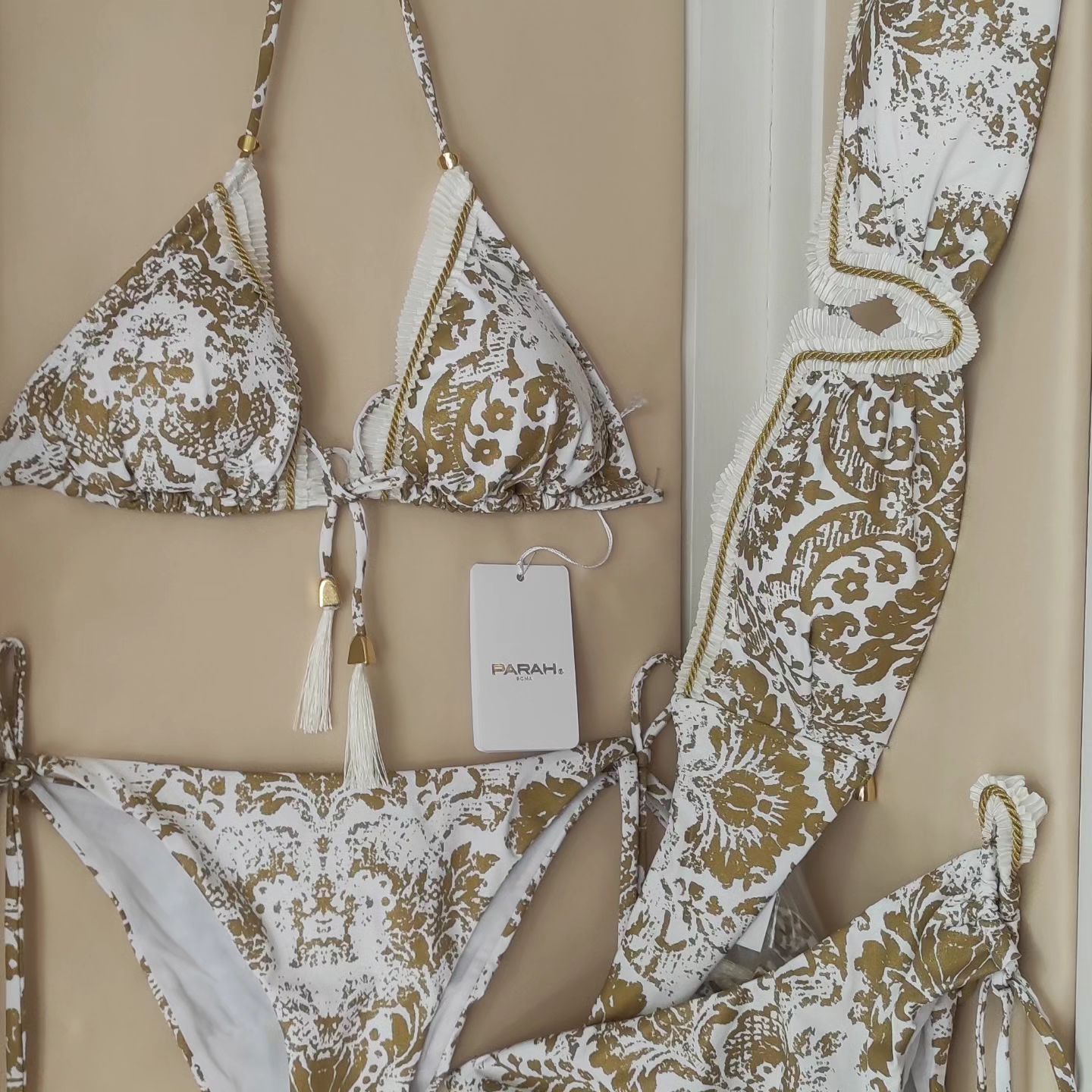 Bikini con stampa damascata bianca e oro su sfondo beige.