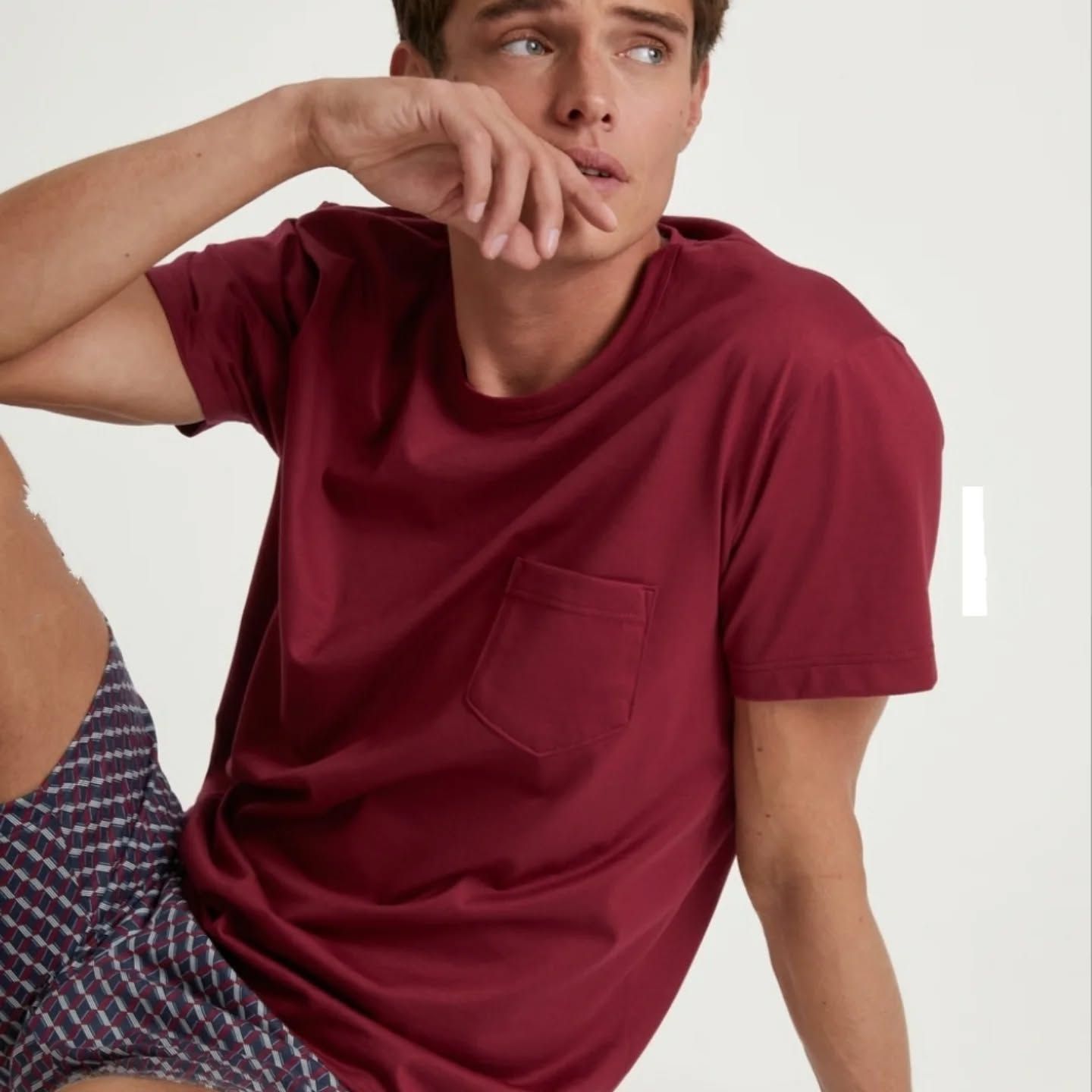 Uomo con maglietta marrone e pantaloncini a fantasia, che si tocca il viso.