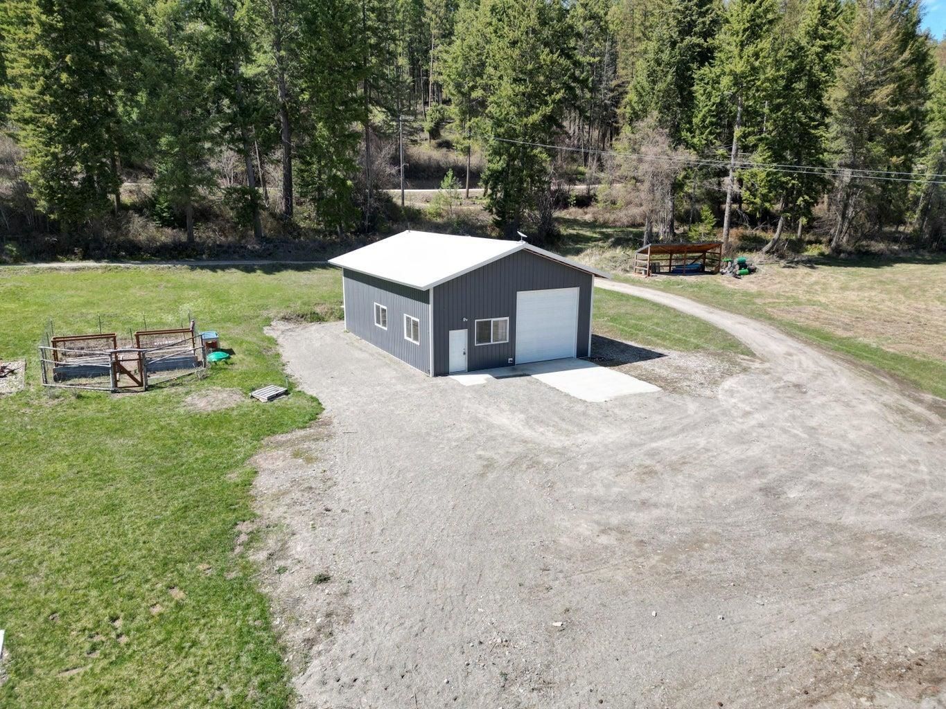 Small gray shed on a gravel clearing beside a grassy yard and forested area.