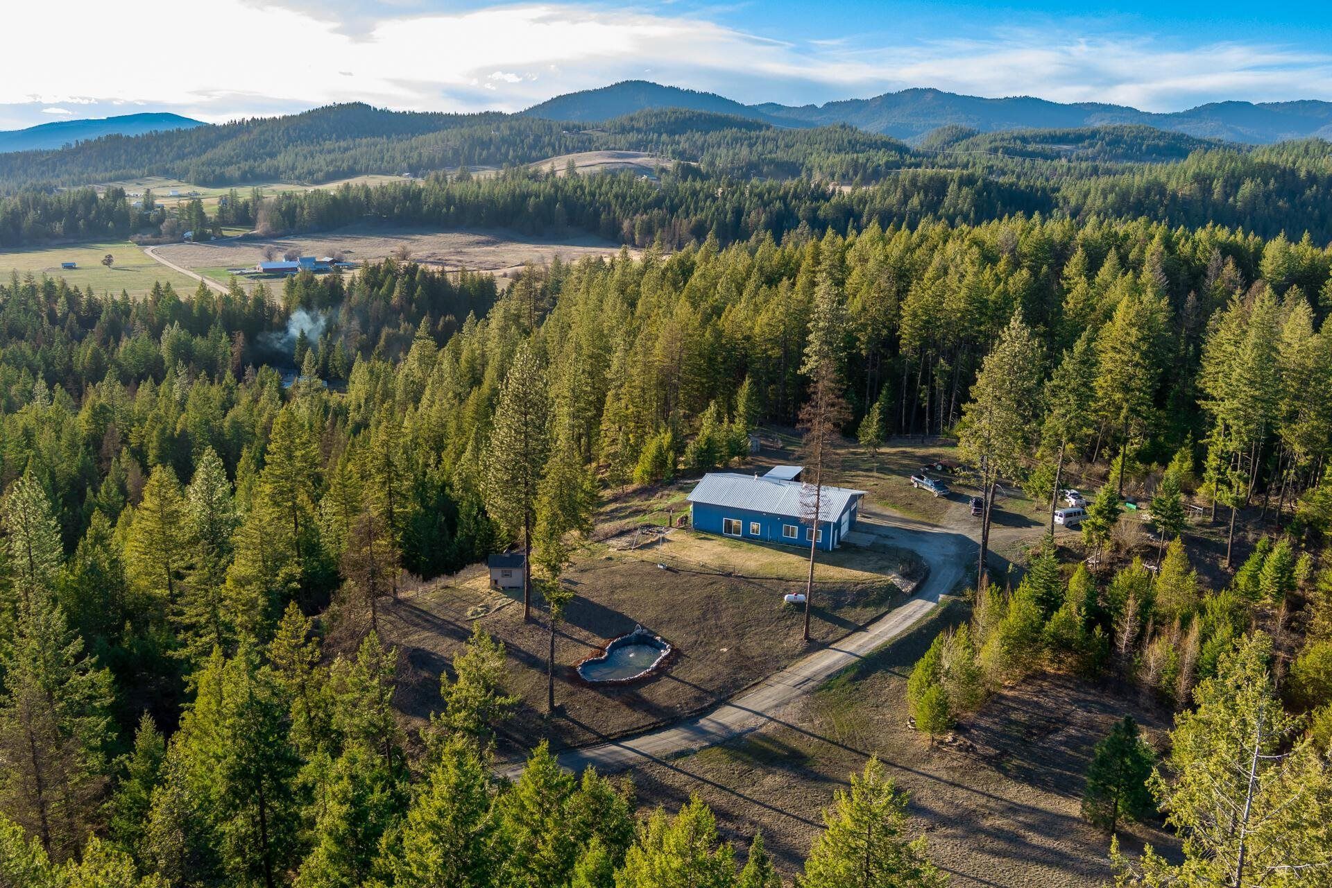 Aerial view of a small white house in a forest clearing with mountains in the distance.