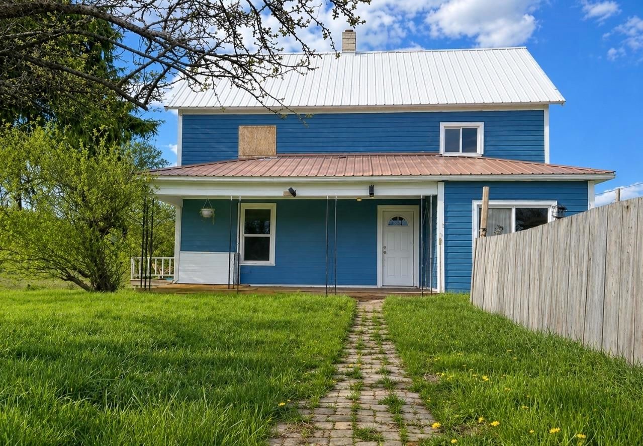 Blue two-story house with a white roof, front lawn, and stone path under a clear sky