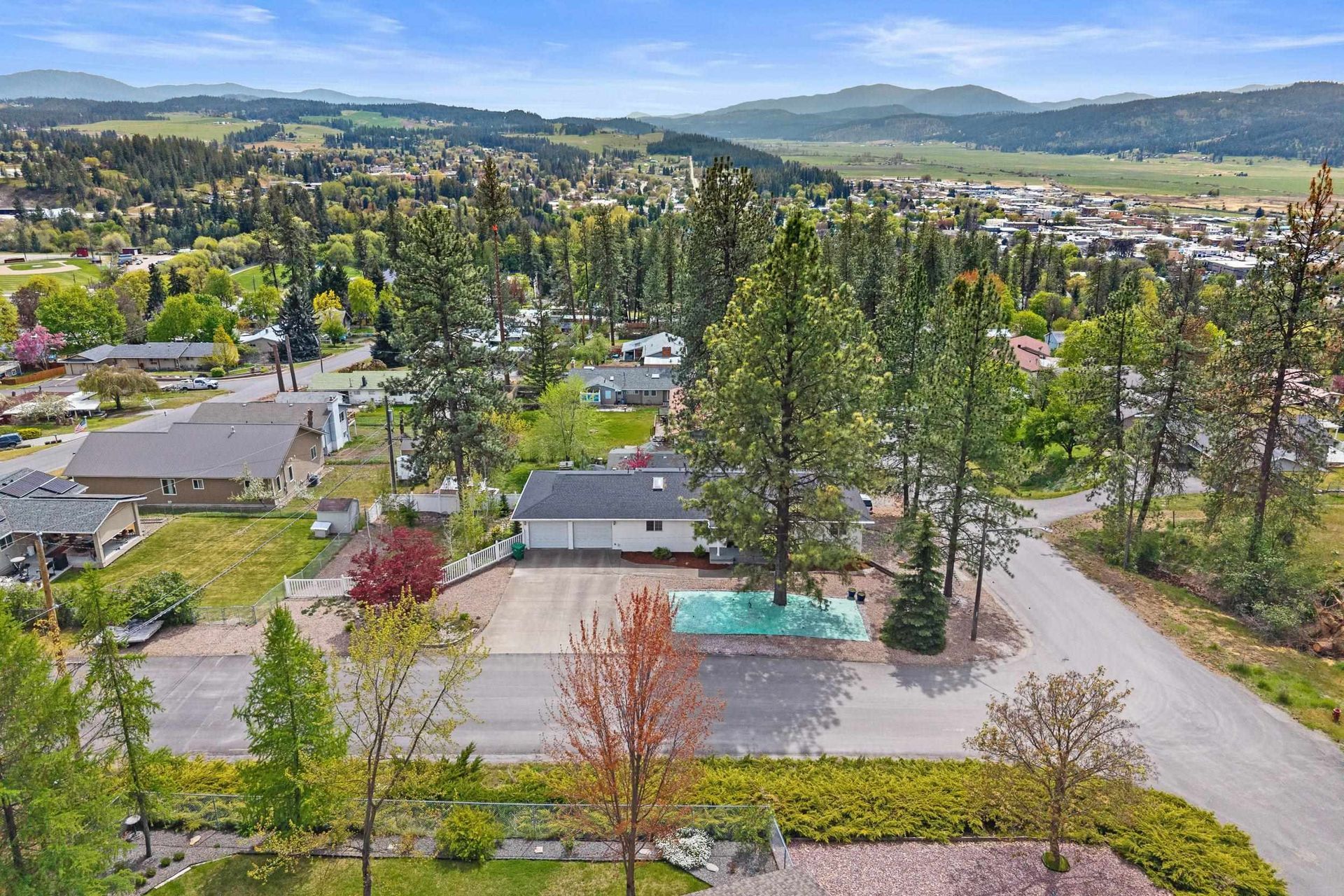 Aerial view of a suburban neighborhood with trees, roads, houses, and distant hills under a clear sky