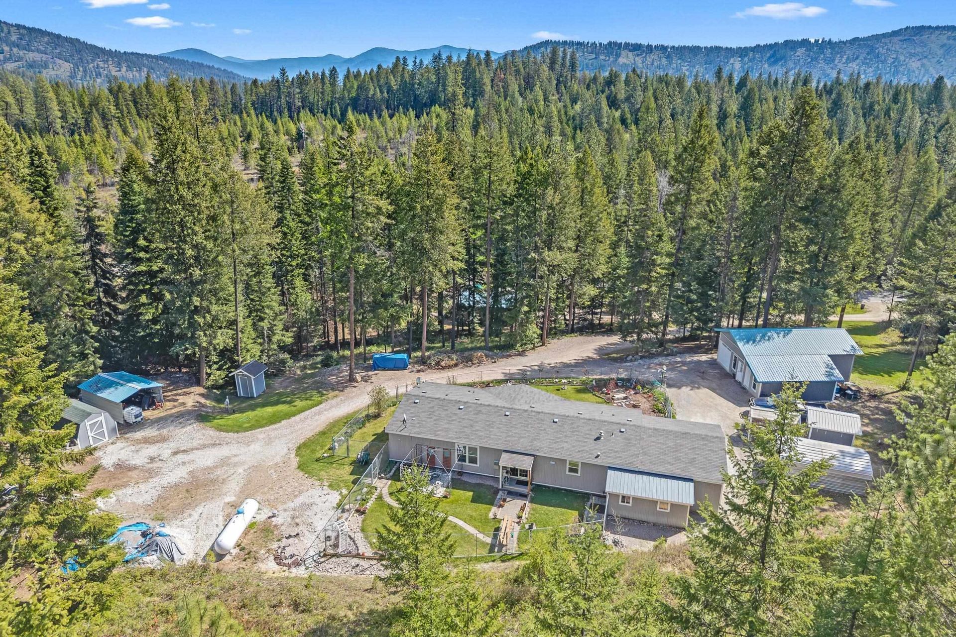 Aerial view of a forested mountain lodge with several buildings and dirt roads surrounded by tall evergreen trees.