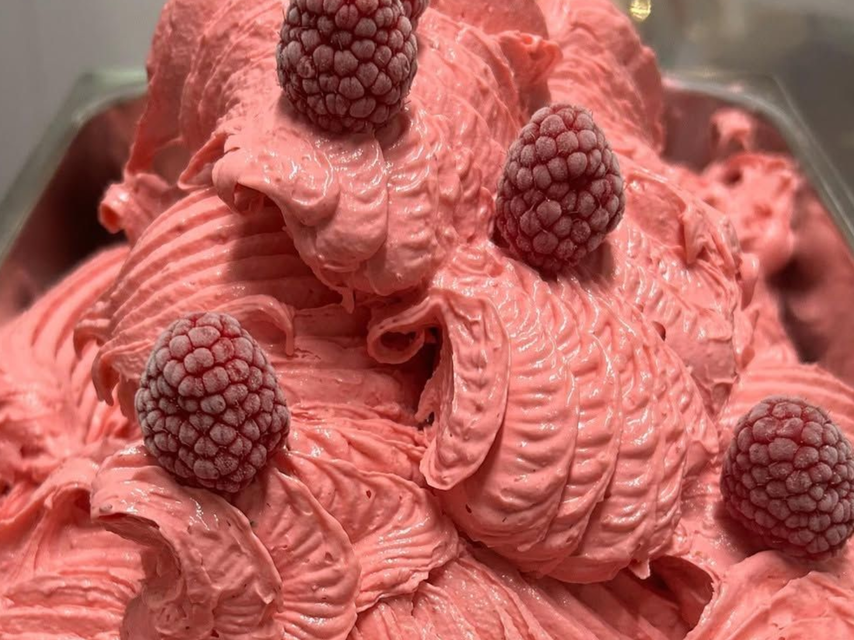 Gelato al lampone rosa guarnito con lamponi interi in un contenitore trasparente.