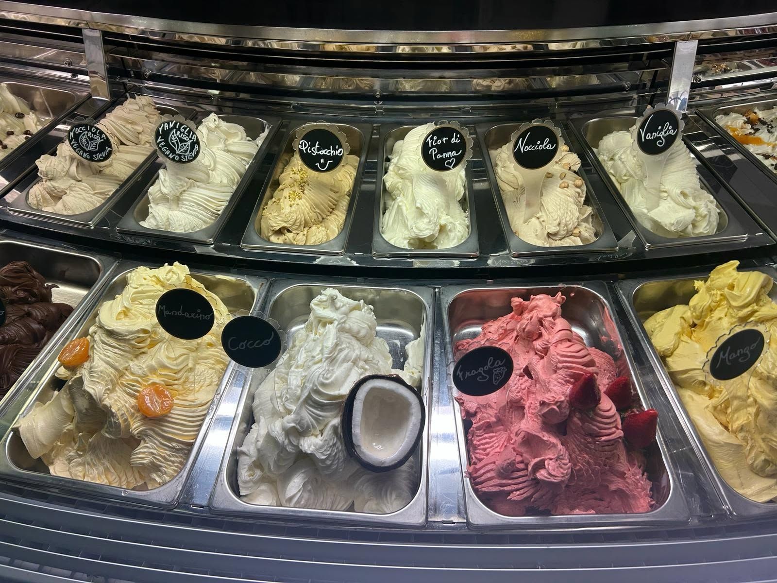 Assortimento di gusti di gelato in una vetrina con palline di gelato alla crema, giallo, rosa e arancione.