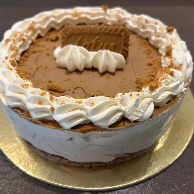 Torta rotonda da dessert con bordo di panna montata, copertura al caramello e decorazione di biscotti su un vassoio dorato.