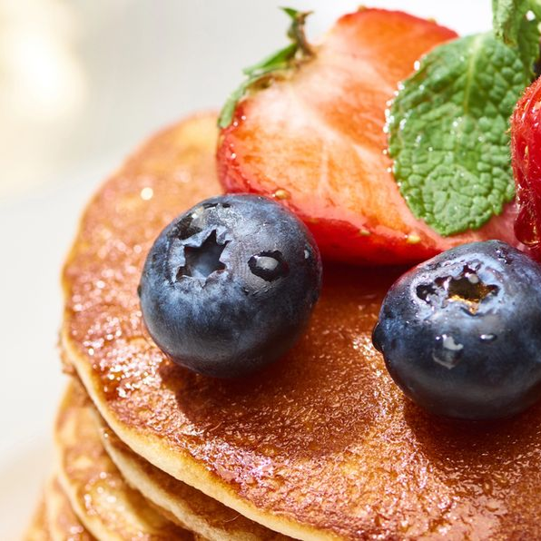Pila di pancake guarnita con mirtilli, fragole a fette e foglie di menta.