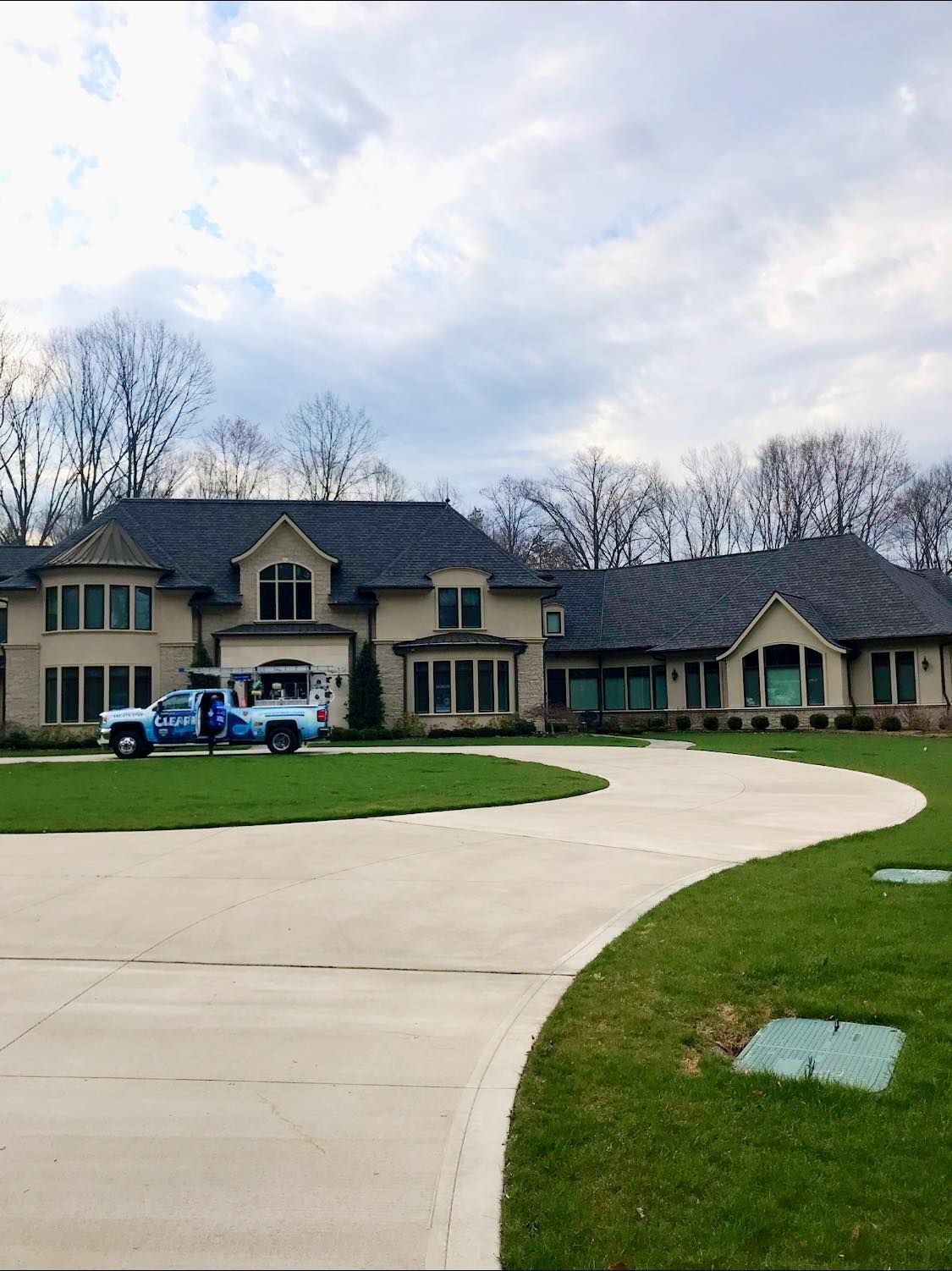 Large beige house with a curved driveway and green lawn. A blue truck is parked in front.