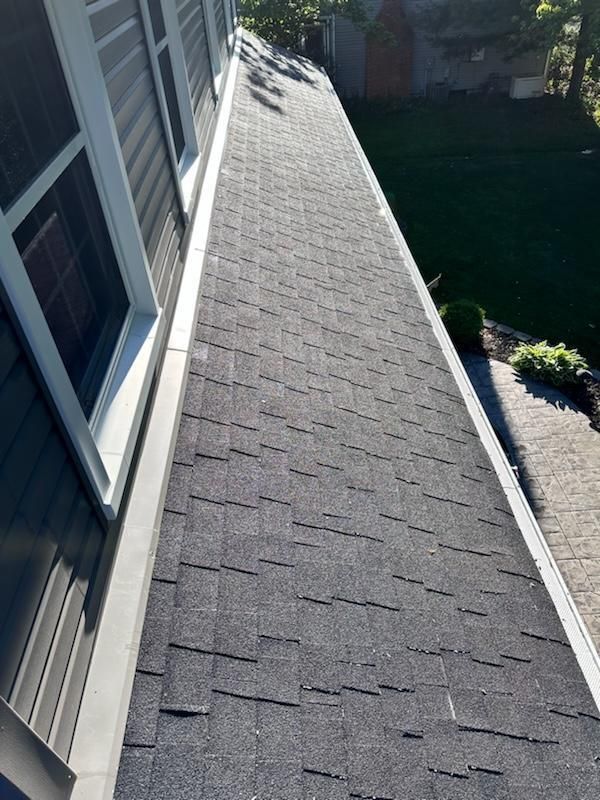 Asphalt shingle roof with gray shingles, gutter, and windows along a house.