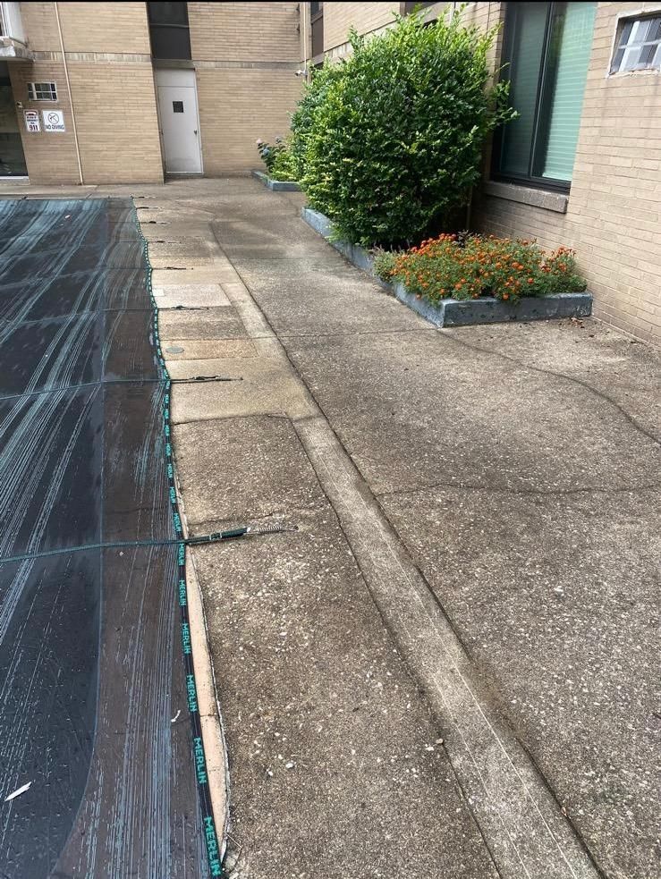 Concrete path next to a planting bed and covered pool. Building in the background.