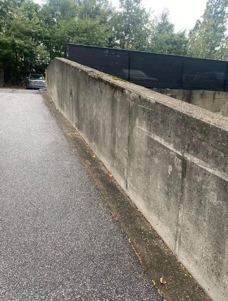 Concrete retaining wall next to an asphalt surface, trees in the background.