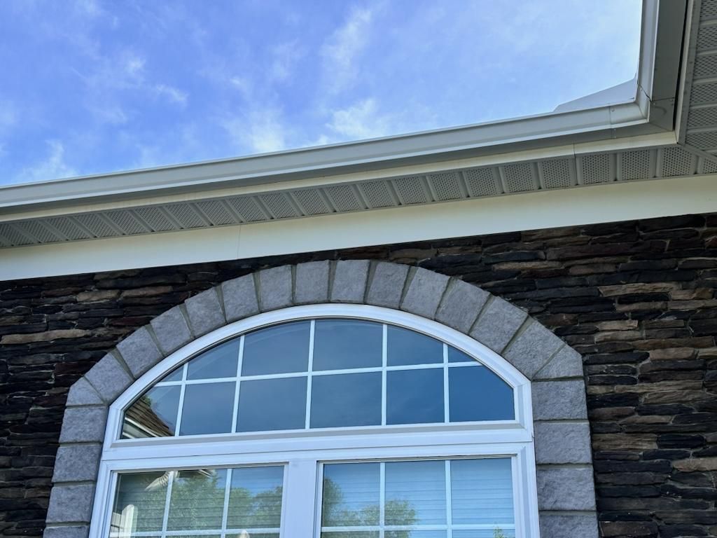 Arched window with stone trim on a brick facade, beneath white trim and a blue sky.
