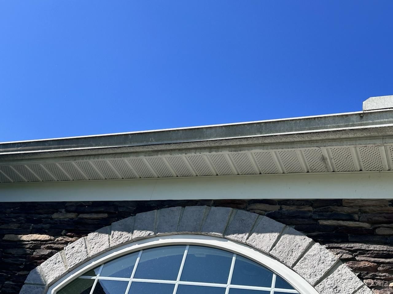 Gutter and soffit on a house with a blue sky background. The house has a stone facade and arched window.