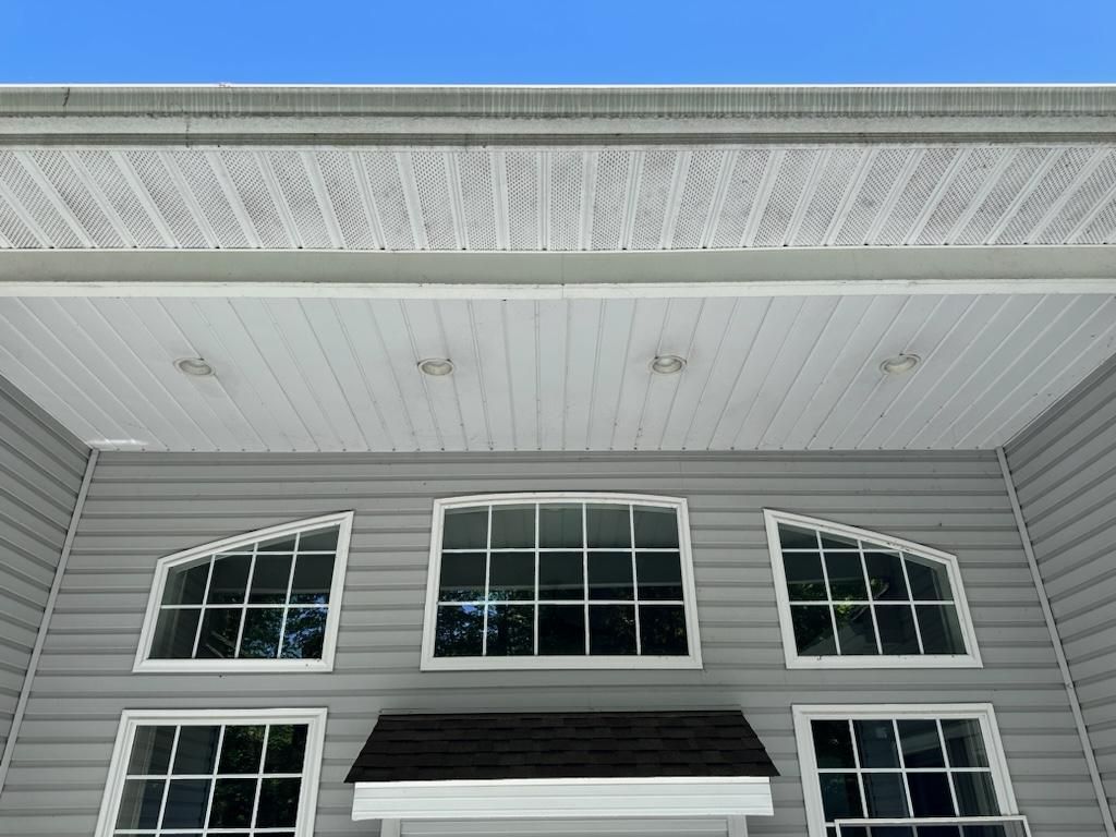 Gray house exterior with windows, soffit, and siding against a blue sky.