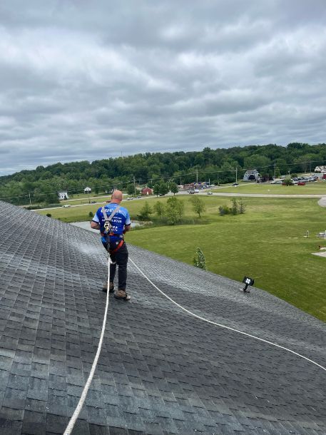 Roofer on a roof wearing safety gear, with a harness and rope, looking at the distance, overcast sky.