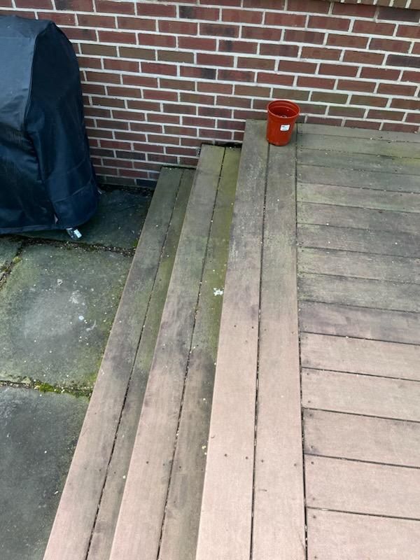 Wooden deck with steps, a brick wall, and a black grill cover. A red bucket sits on the deck.
