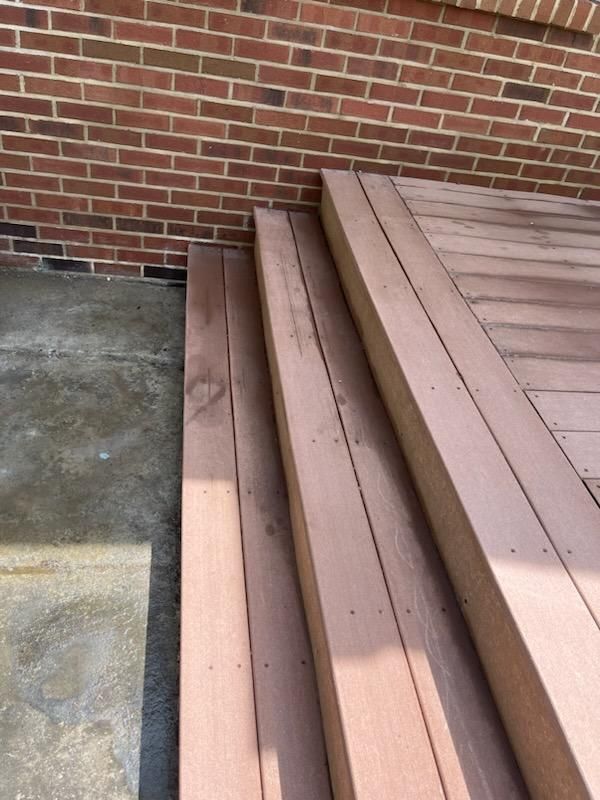 Wooden deck with steps next to a brick wall. Concrete surface on left.