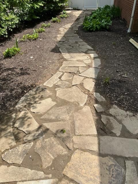 Stone pathway winding through a garden, leading to a white gate.