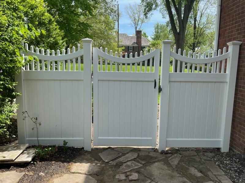 White picket fence with three connected gates, set on a stone patio in a yard.