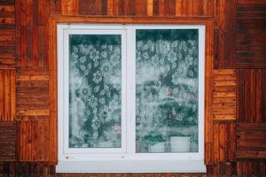 White-framed window with floral curtains in a wooden cabin wall.