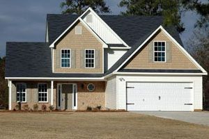 Two-story house with tan siding, white trim, and a dark gray roof. Includes a two-car garage.