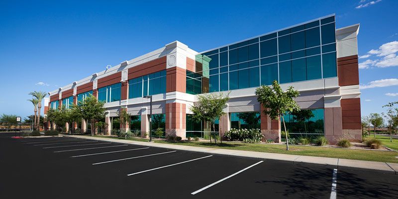 Office building with large glass windows and a parking lot. Blue sky in the background.