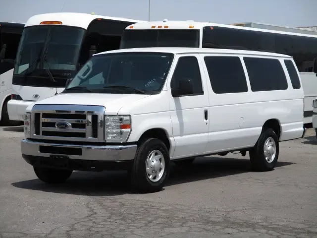 Dark blue sedan parked on a concrete surface, with a chain link fence and buildings in the background.