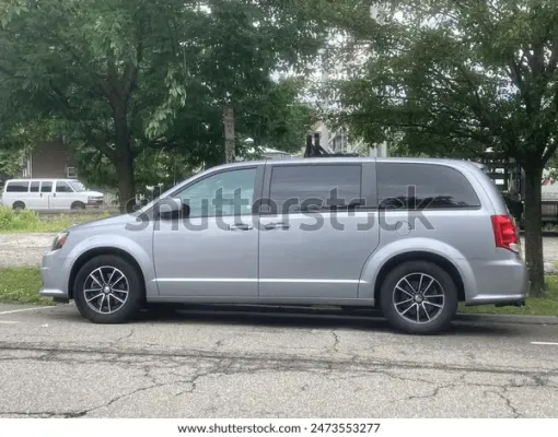 White VW camper van driving on a city street; a person inside, a pedestrian on the side.