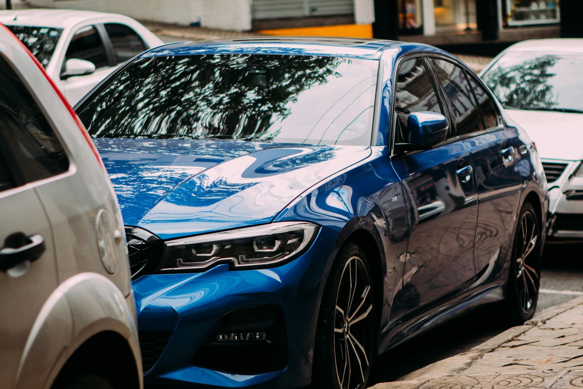 Blue sedan parked on a city street, partially obscured by other vehicles.